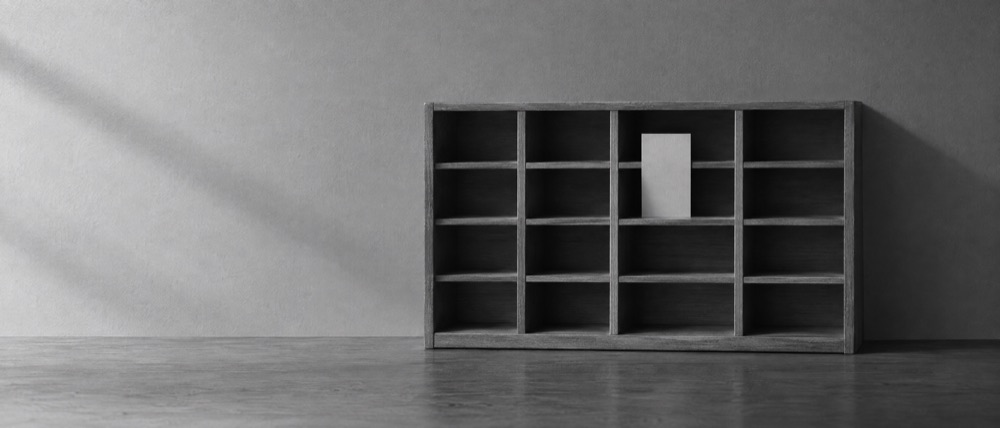 Photograph, greyscale: a wooden docket shelf of empty compartments with a single blank card in one of them